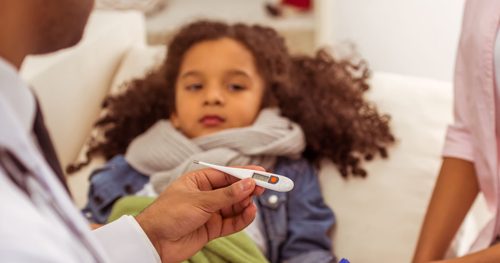doctor holding a thermometer, in the background cute little girl lying in bed ill